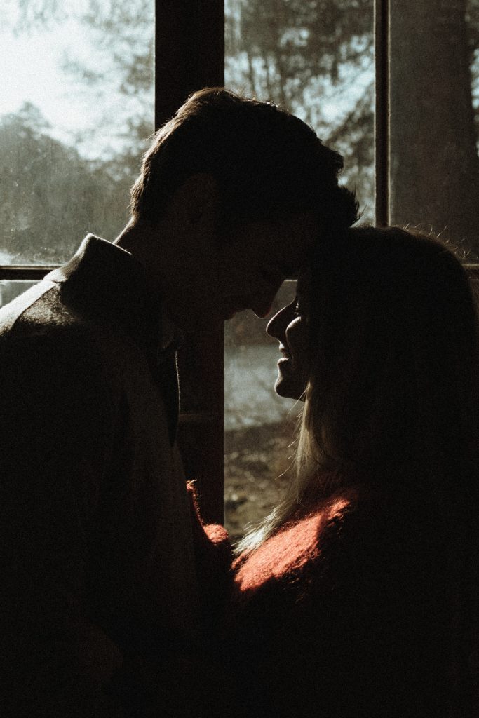 Moment de tendresse en couple pendant une séance engagement en Moselle. Ils sont front contre front devant la fenêtre