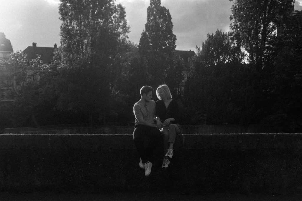 Séance engagement à Metz. Un couple est assis sur un muret et se regarde en se tenant la main