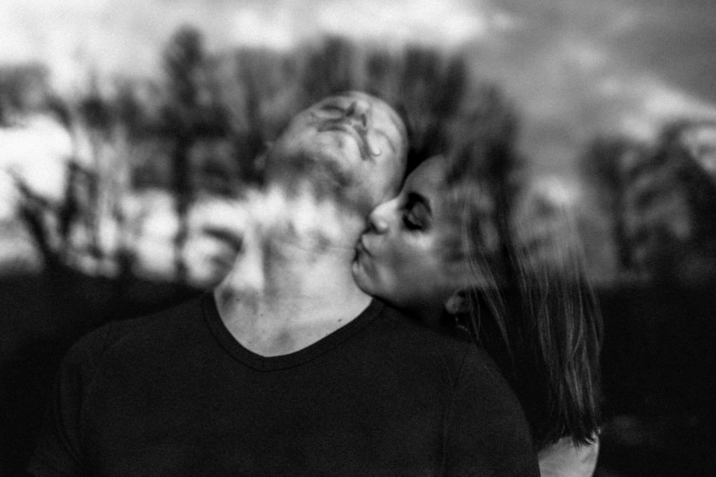 Moment intime en couple, la femme embrasse son mari dans le cou. Les arbres se reflètent dans la fenêtre