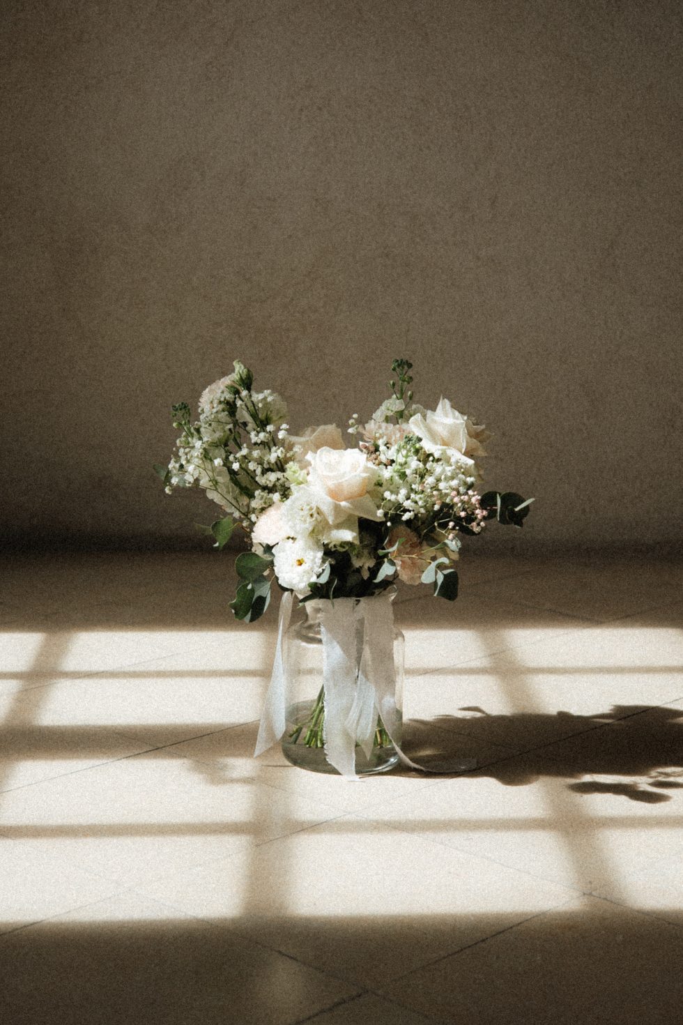 Un bouquet de roses et gypsophiles dans un vase posé sur le sol de l'Abbaye des Prémontrés. Le bouquet est baigné par la lumière qui passe par la fenêtre
