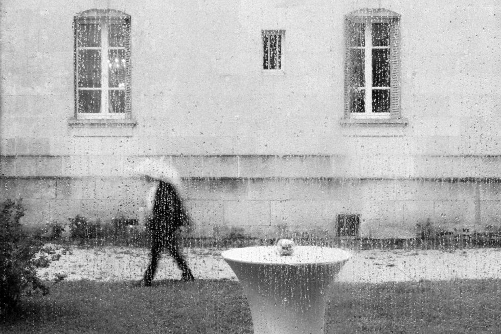 Scène de mariage sous la pluie pendant le cocktail au Château des Aulnes, vue à travers une vitre mouillée