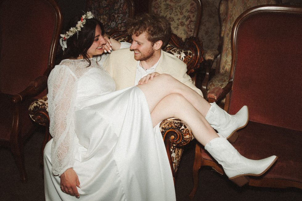 Photo de couple pendant la soirée au Petit Château de Seicheprey. Les mariés sont assis dans un fauteuil ancien et échangent un regard complice.