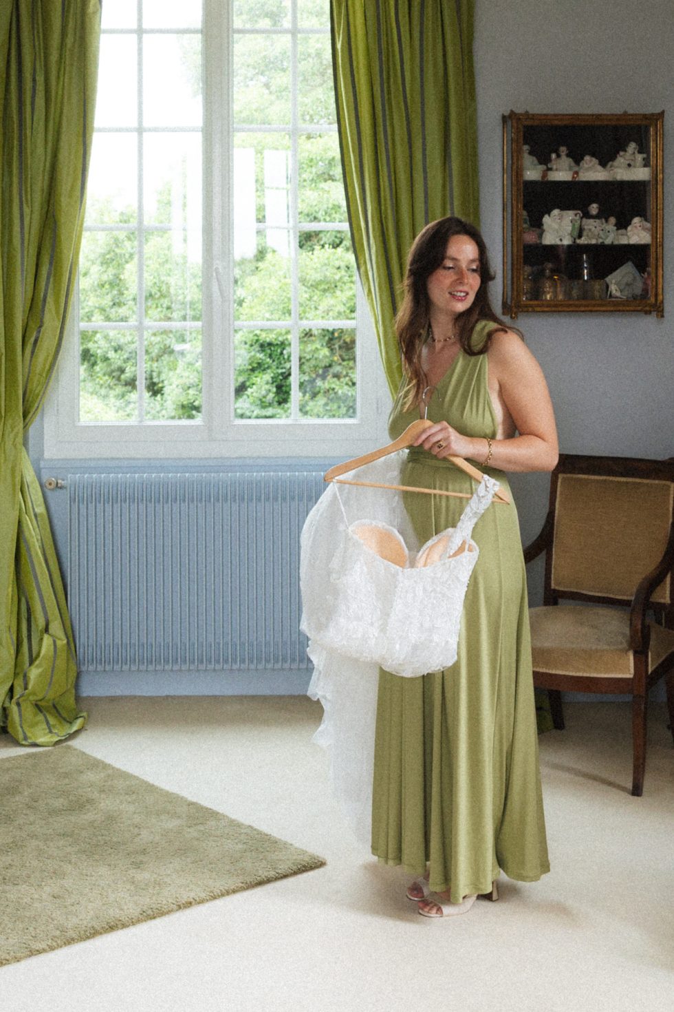 La demoiselle d'honneur tenant la robe de mariée est dans ses pensées. Elle est dans la chambre nuptiale au Domaine de Millanges. Sa robe est assortie aux ridaux