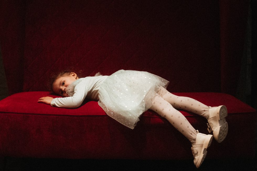 Petite fille allongée sur un canapé rouge, perdue dans ses pensées au milieu de la fête au Schengener Haff