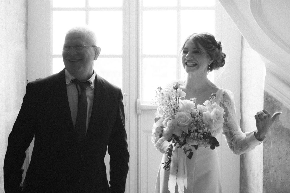 La mariée et son beau-père sourient. Ils s'apprêtent à entrer dans la salle de la cérémonie laïque