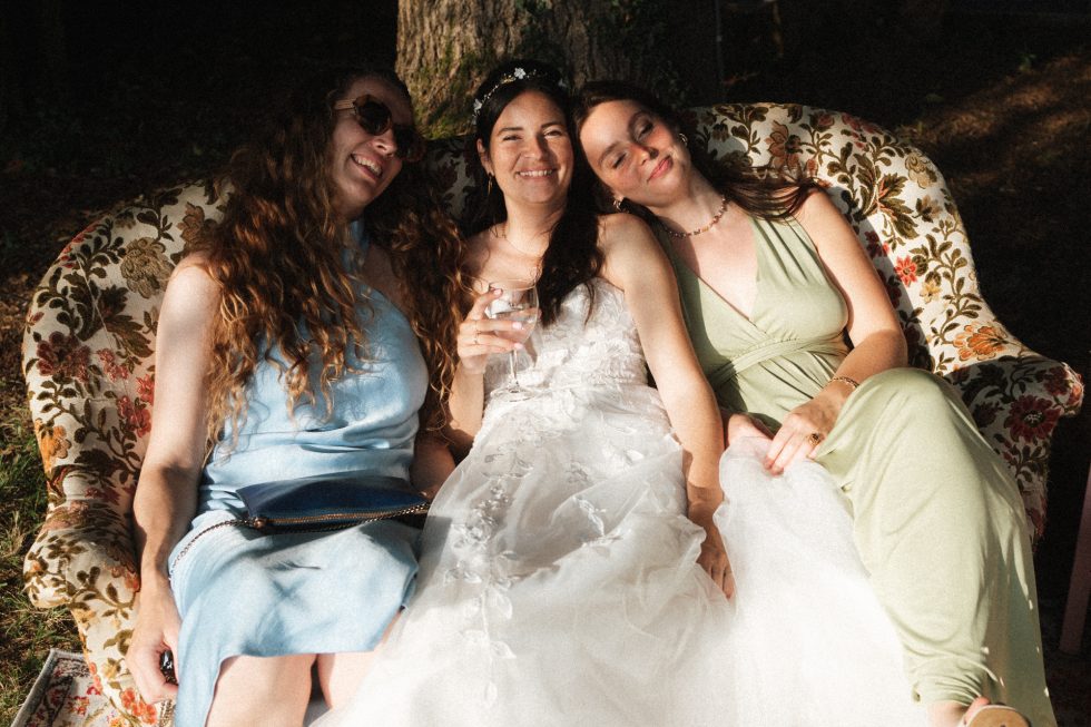La mariée partage un moment complice avec ses amies, assises au soleil sur un canapé fleuri au Domaine de Millanges à Tabanac.