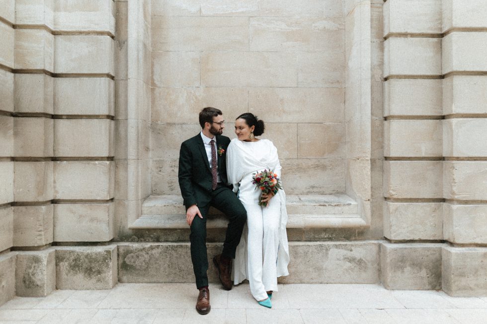 Séance couple le jour du mariage à Nancy. Les mariés, assis sur un muret, échangent un regard complice