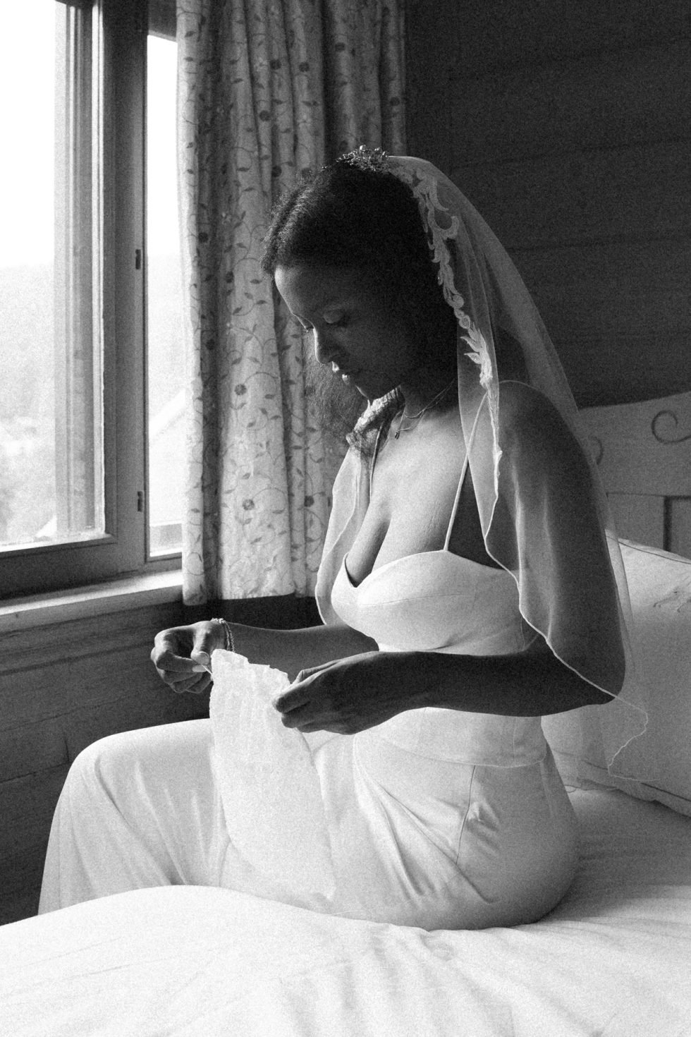 Portrait d'une mariée dans la chambre d'hôtel au Jardins de Sophie. Elle est assise sur le lit.