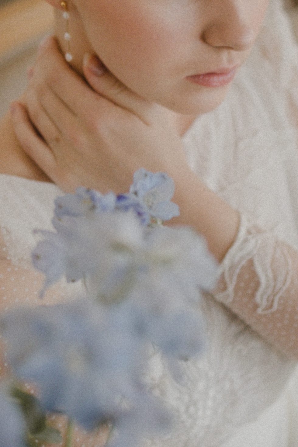 Détail délicat de la mariée, main posée sur son cou, entourée de delphiniums en avant-plan au Château d'Art-sur-Meurthe