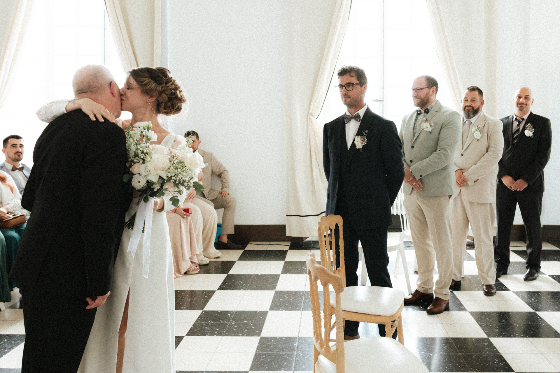 Arrivée de la mariée pendant la cérémonie laïque sous les yeux de son futur époux et de ses témoins. Elle embrasse en beau-père