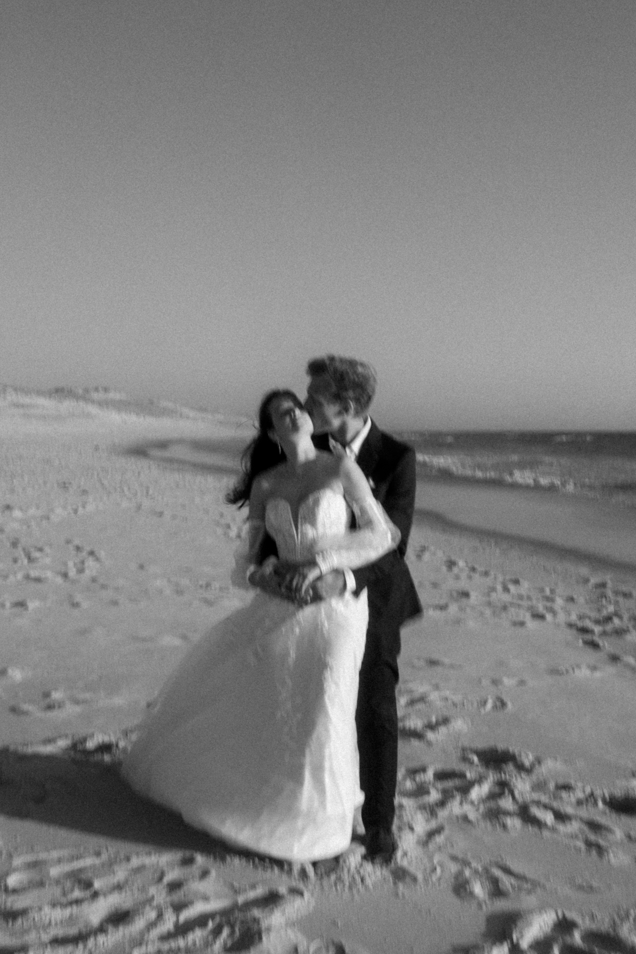 Séance day after à Lacanau Océan. Le mariée tient son épouse par la taille et l'embrasse dans le cou