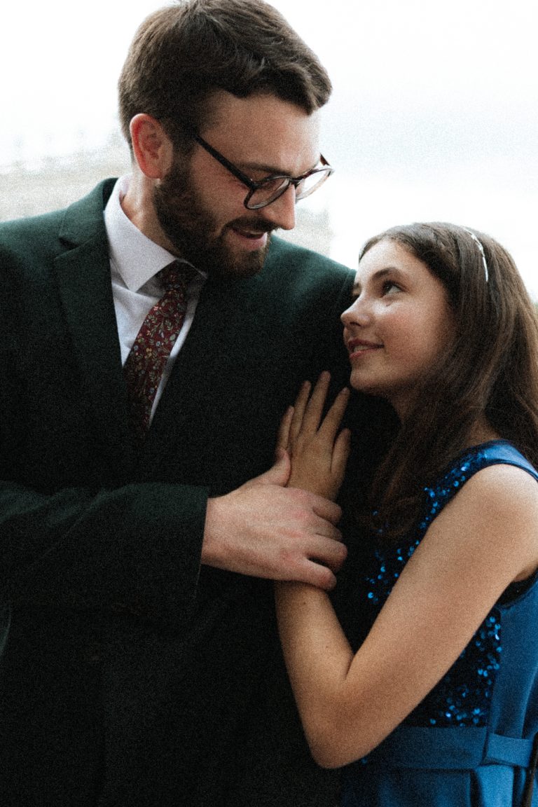 Moment de complicité entre le marié et sa petite sœur. Ils échangent un regard affectueux en se tenant la main. Sur la place Stanislas à Nancy