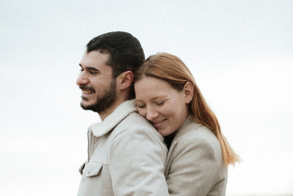 Séance engagement dans les Vosges. La femme enlace son conjoint, ils sourient