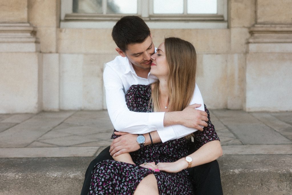 Couple assis sur les marches du Palais du Gouvernement à Nancy pendant une séance engagement. Ils s'enlacent et s'apprêtent à s'embrasser