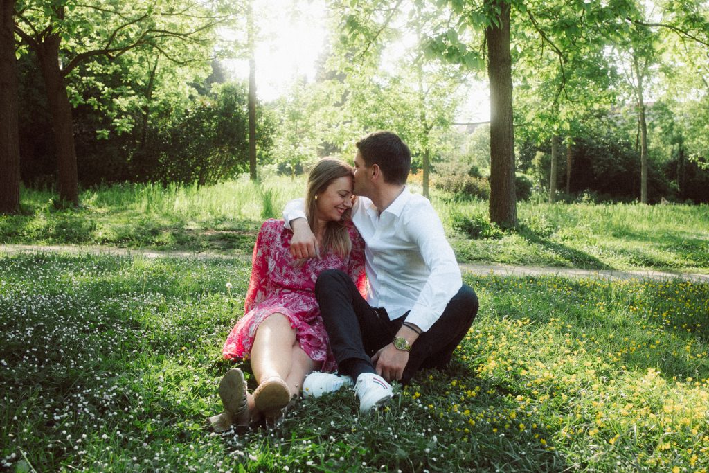 Séance engagement au Parc de la Pépinière à Nancy. Le couple est assis dans l'herbe et l'homme embrasse sa future femme sur le front