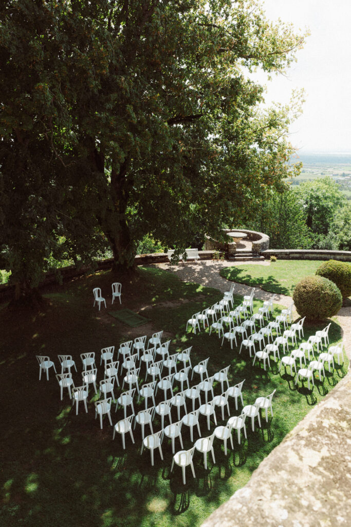 Installation de cérémonie laïque au Château de Hattonchâtel avec rangées de chaises blanches sous un grand arbre dans un jardin verdoyant