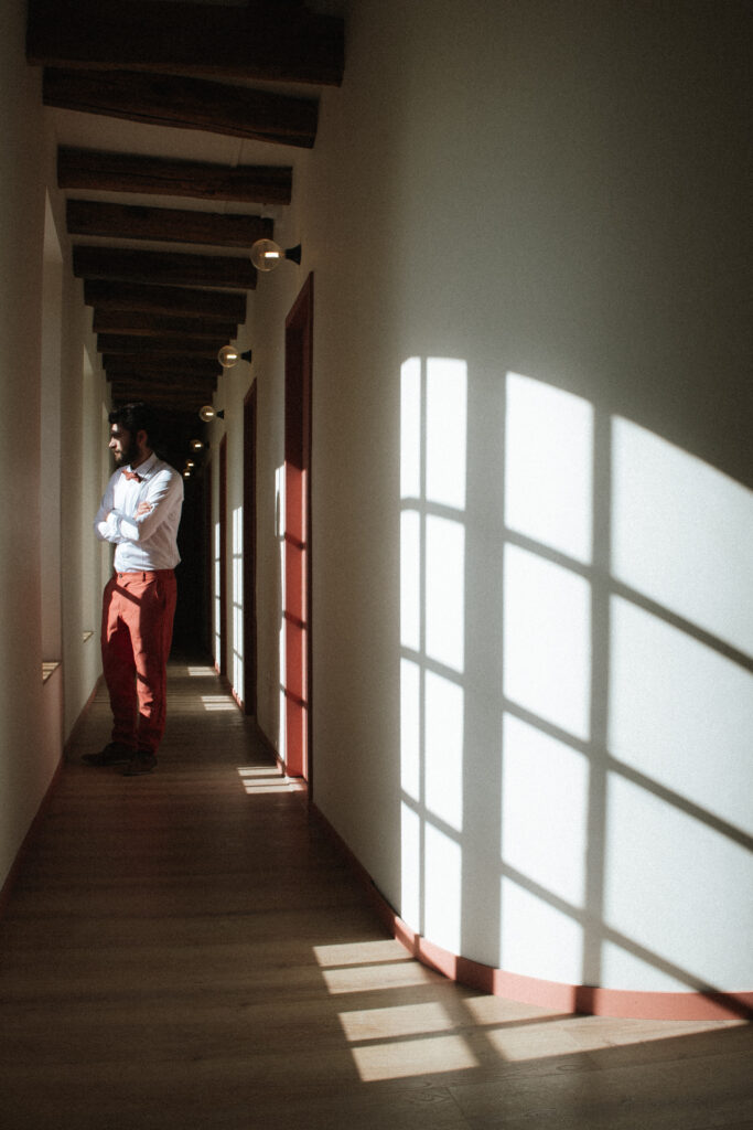 Homme élégant dans un couloir lumineux du Château Ferme d’Aboncourt, jeux d’ombres et lumière sur les murs et le parquet