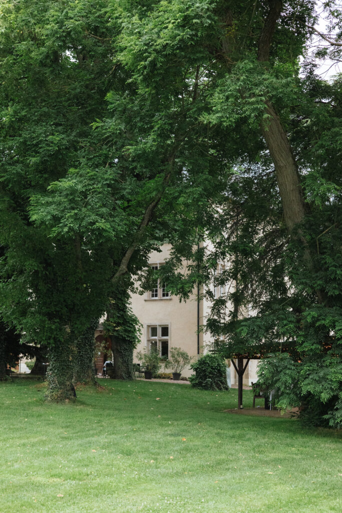Jardin verdoyant du Château de Morey avec pelouse soignée et grands arbres encadrant la façade élégante