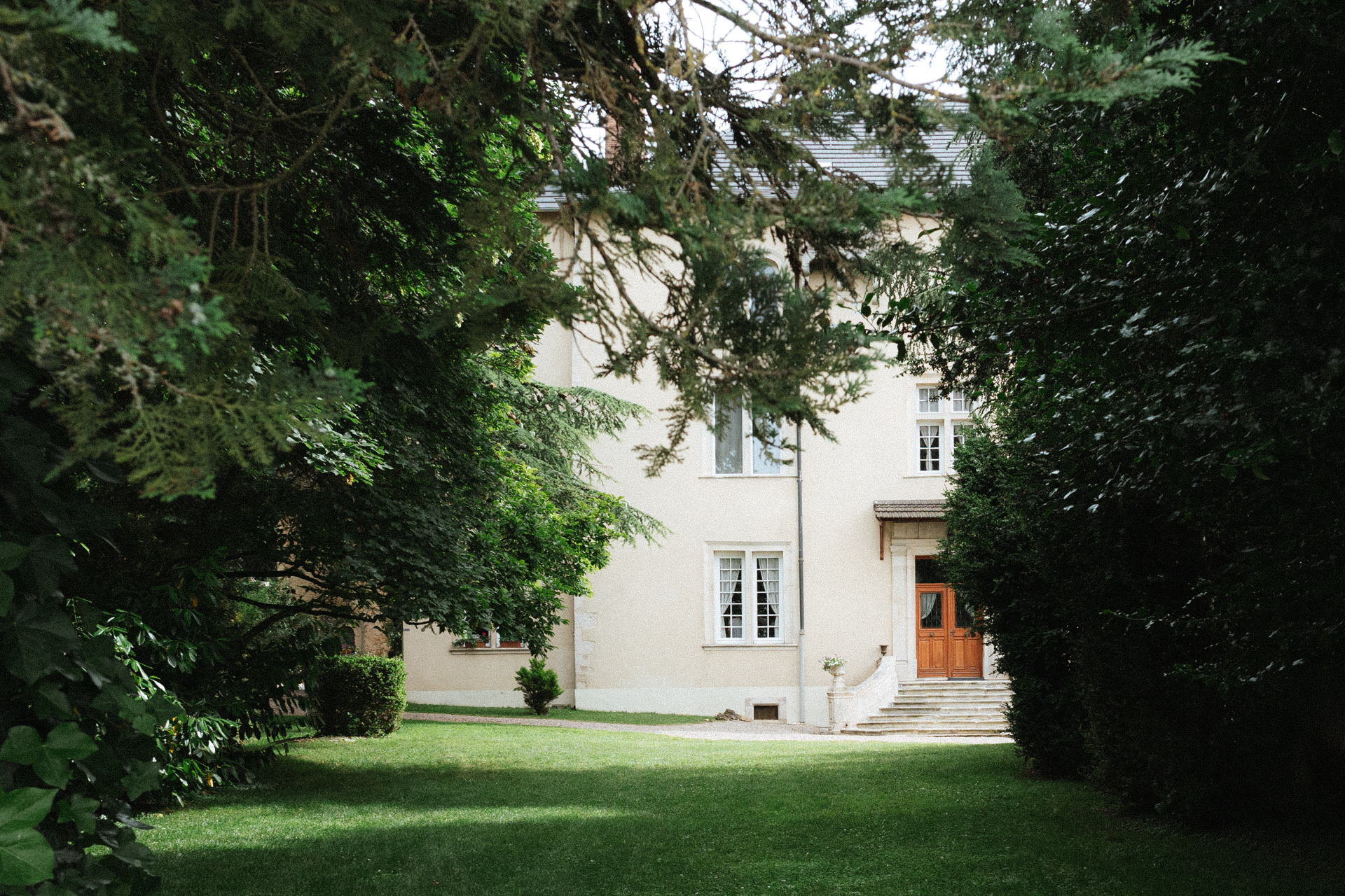 Espace arboré menant à la façade du Château de Morey, entourée d’une végétation dense et d’un parc paisible