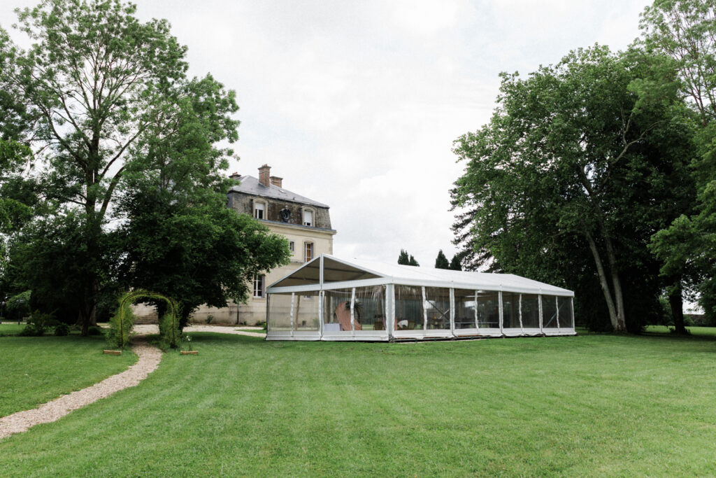 Chapiteau de réception installé dans le parc du Château des Aulnes avec vue sur le château la pelouse verdoyante et les grands arbres