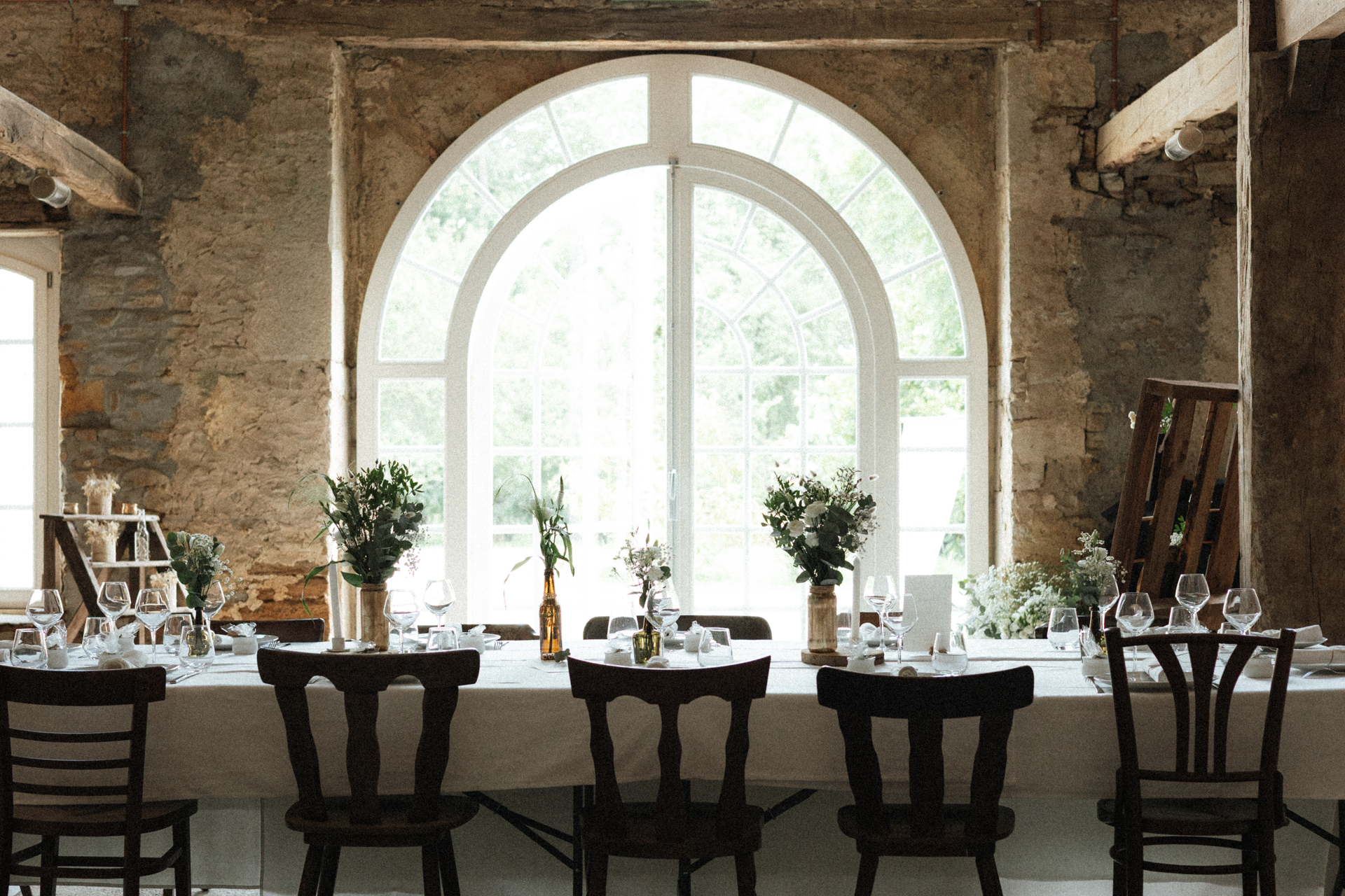Table de mariage décorée dans une salle rustique avec pierres apparentes et grandes fenêtres au Château-Ferme d’Aboncourt