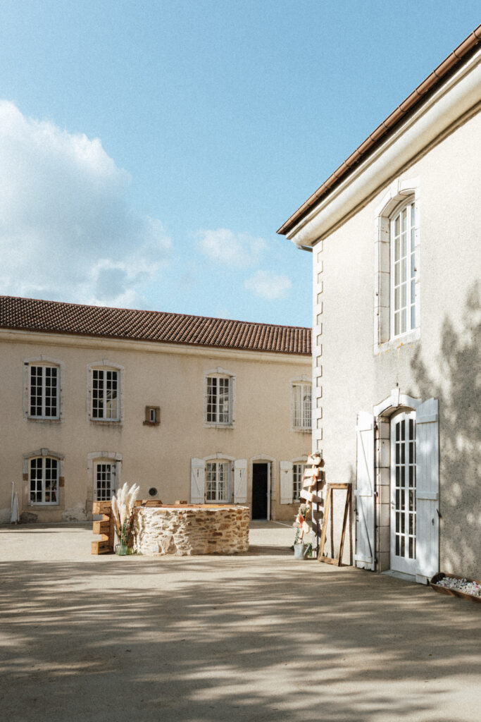 Cour extérieure lumineuse du Château-Ferme d’Aboncourt avec bâtiment en pierre et ciel dégagé le jour d'un mariage