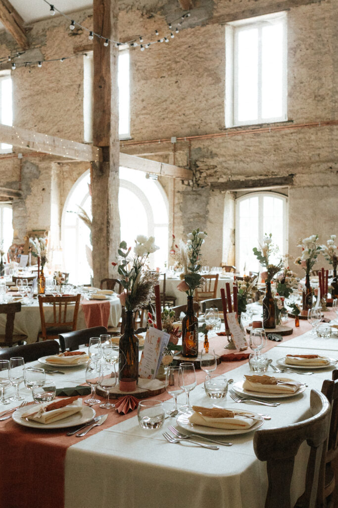 Tables de réception décorées avec bougies et fleurs dans la salle de réception au Château-Ferme d’Aboncourt lors d'une journée de mariage