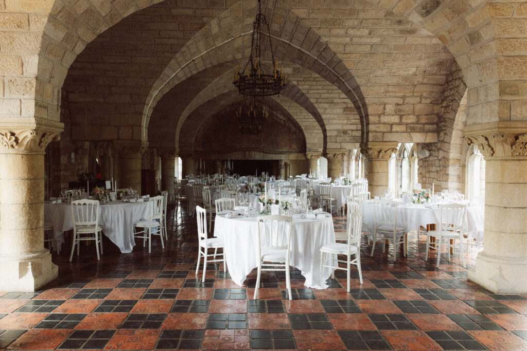 Grande salle de réception voûtée du Château de Hattonchâtel avec tables rondes et décoration de mariage raffinée