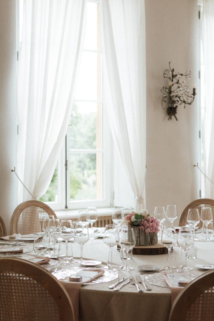 Table de réception lumineuse avec verrerie fine et centre de fleurs pastel près d’une fenêtre au Château de Schengen au Luxembourg
