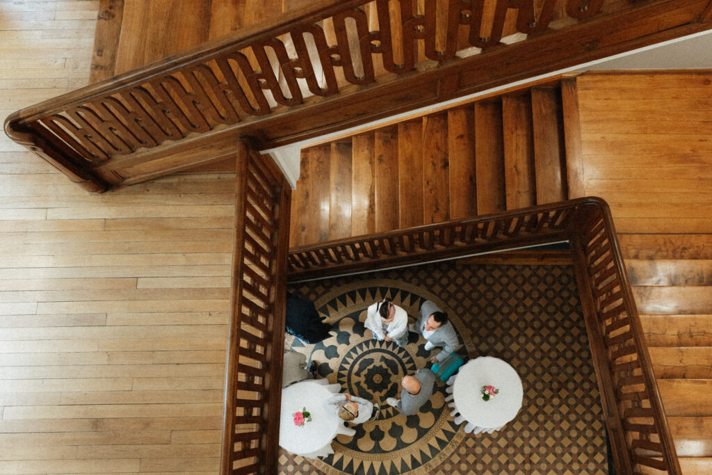 Vue plongeante sur un escalier en bois et sol à motifs avec invités réunis autour de tables au Château de Schengen au Luxembourg
