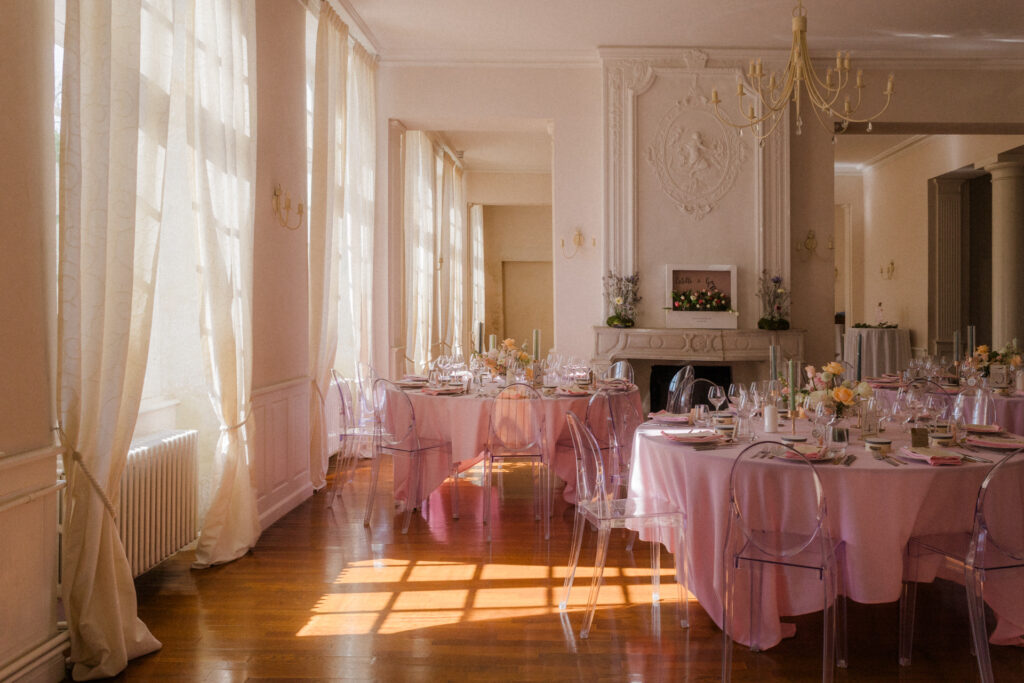 Salle de réception avec tables nappées de rose, chaises transparentes et décoration florale au Château de Vandeléville