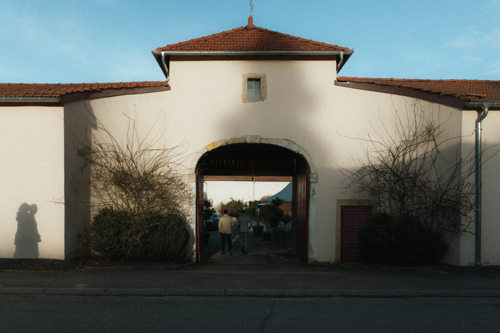 Entrée du Domaine de Raville avec arche et invités arrivant, lumière dorée en fin de journée.