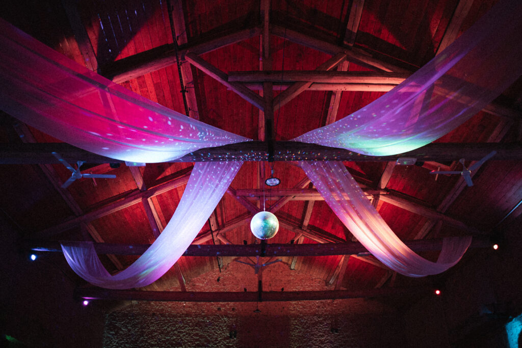 Plafond de salle de réception au Domaine de Raville décoré de voilages et lumières colorées pour soirée de mariage