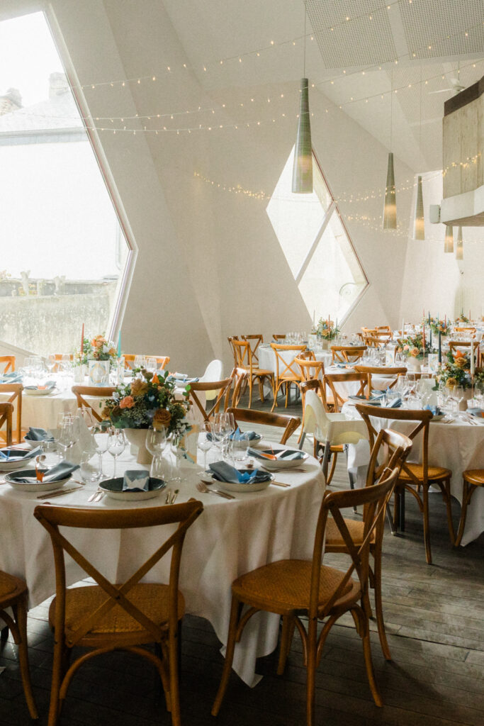Salle de réception contemporaine avec grandes baies vitrées graphiques, guirlandes lumineuses et tables décorées au Schengener Haff au Luxembourg