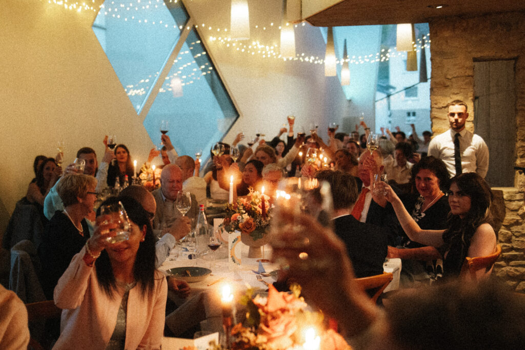 Invités levant leurs verres lors d’un repas de mariage à la lumière des bougies dans la salle de réception du Schengener Haff au Luxembourg