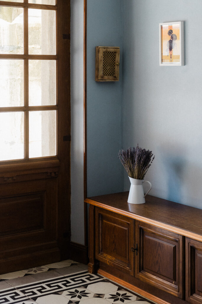 Entrée intérieure élégante avec porte vitrée, meuble en bois, carrelage graphique noir et blanc et bouquet de lavande au Petit Château de Seicheprey