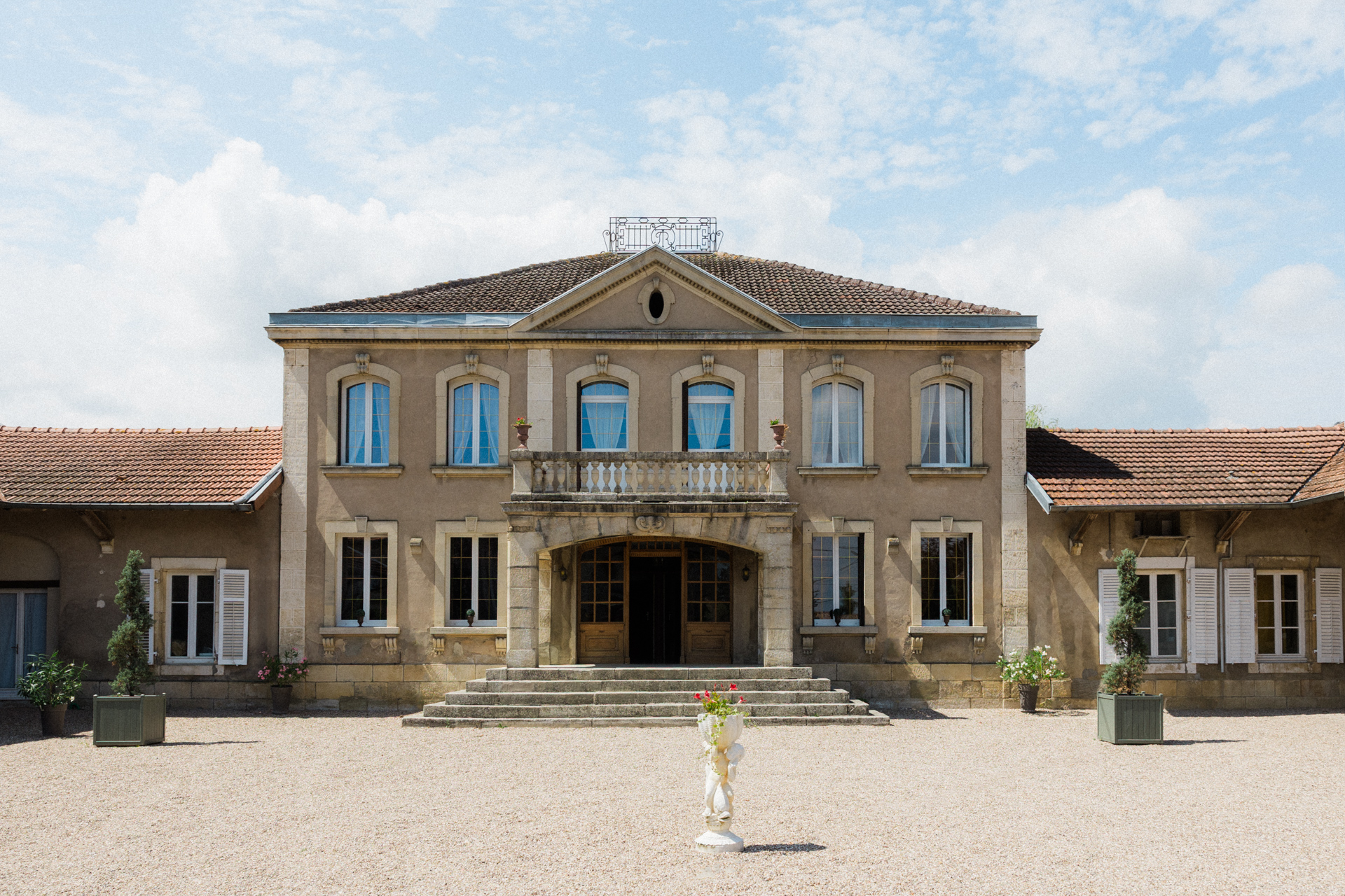 Façade symétrique du Petit Château de Seicheprey avec escalier central et cour gravillonnée sous ciel lumineux