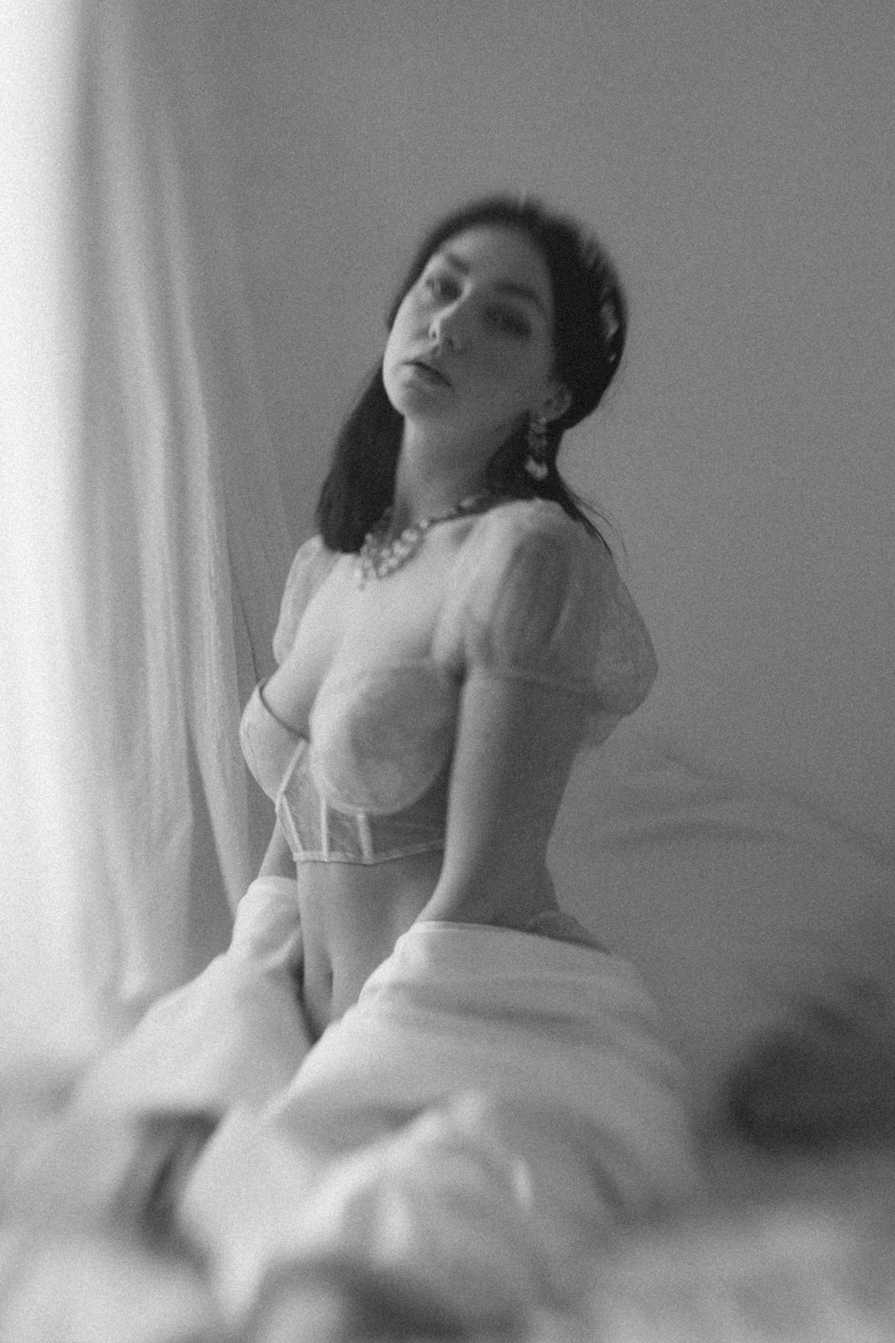 Séance boudoir de la mariée artistique. La mariée est assise sur le lit avec son voile autour de sa taille.