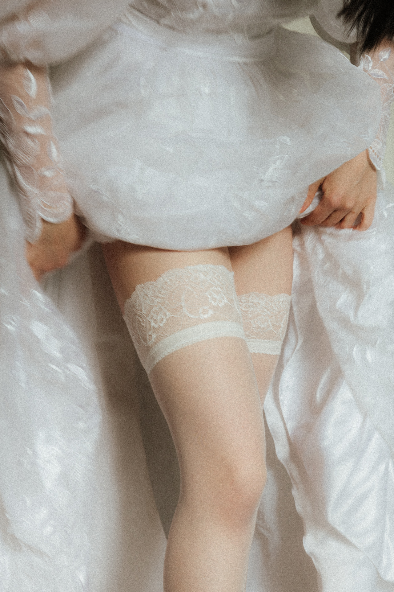 Séance boudoir de la mariée en bas blancs et robe vaporeuse, détail élégant de lingerie dans une ambiance lumineuse.