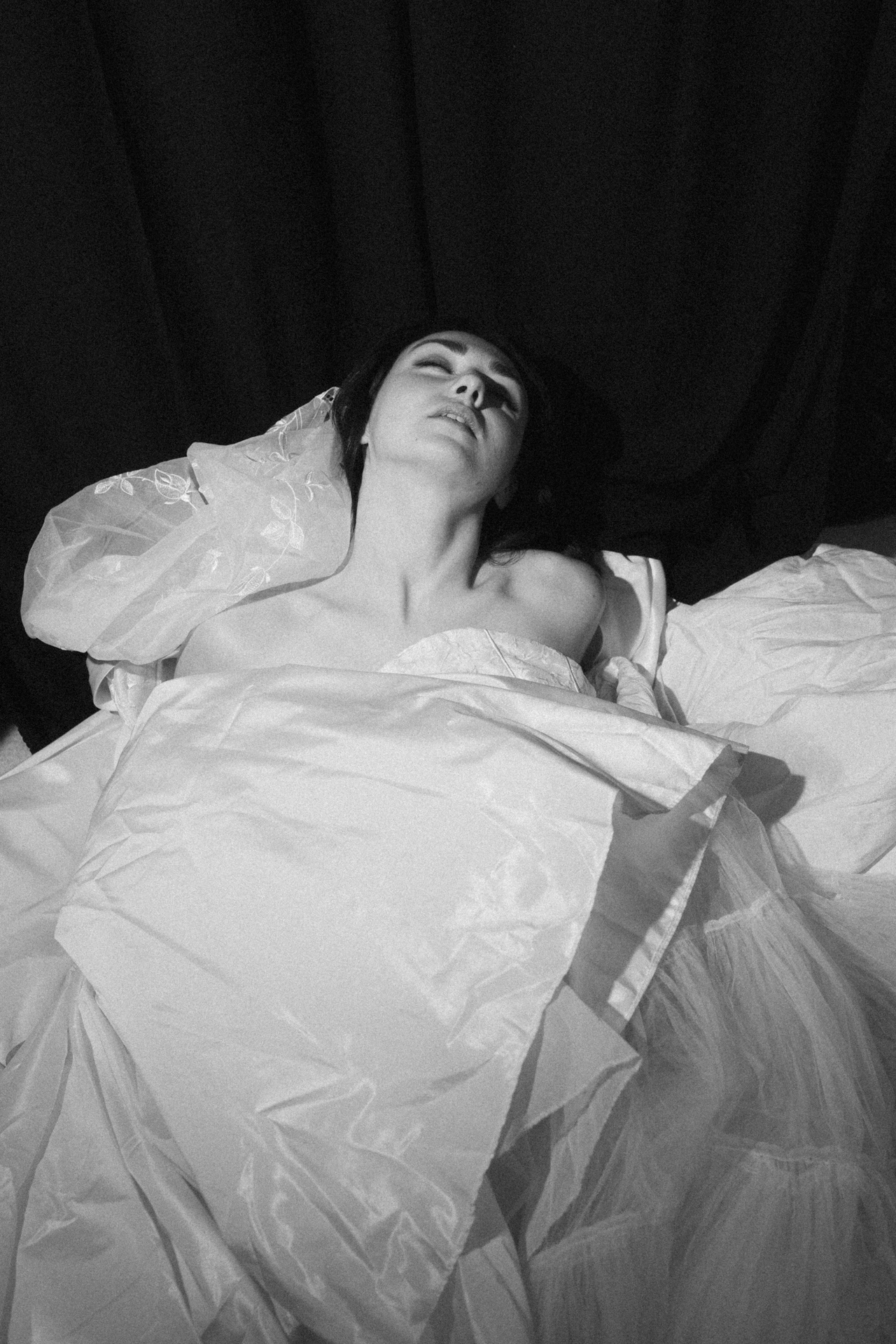 Portrait noir et blanc d’une mariée allongée dans son voile, dans une ambiance éditoriale. Pendant une séance boudoir de la mariée