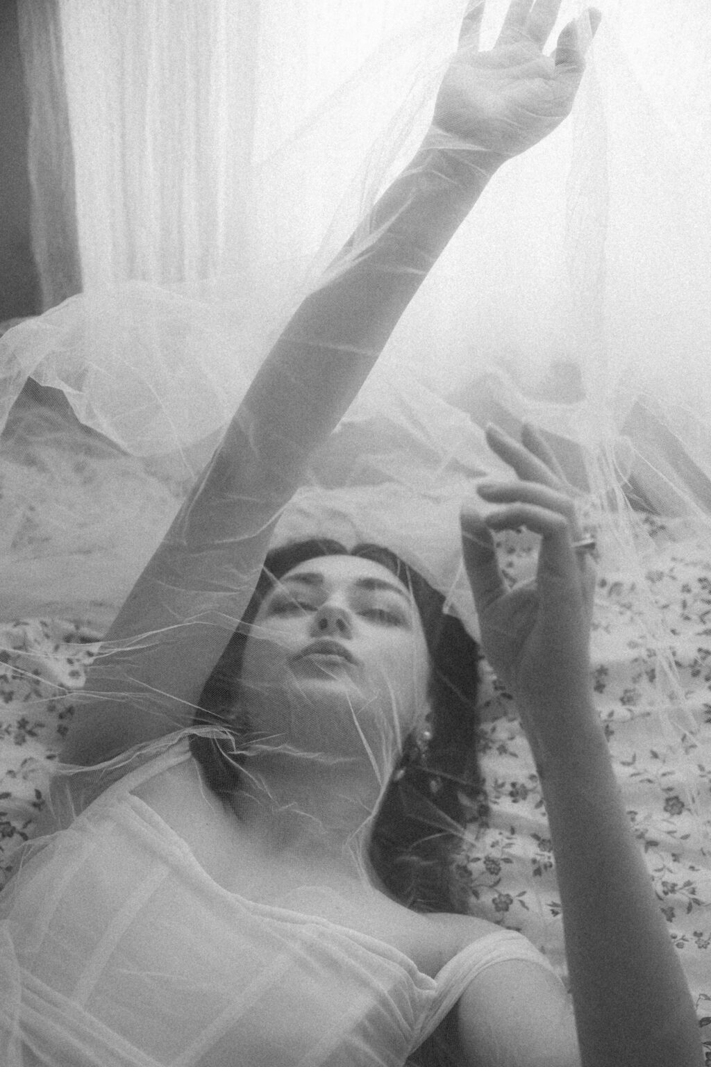 Portrait intime d'une mariée en lingerie blanche, jouant avec son voile transparent pendant une séance boudoir de la mariée