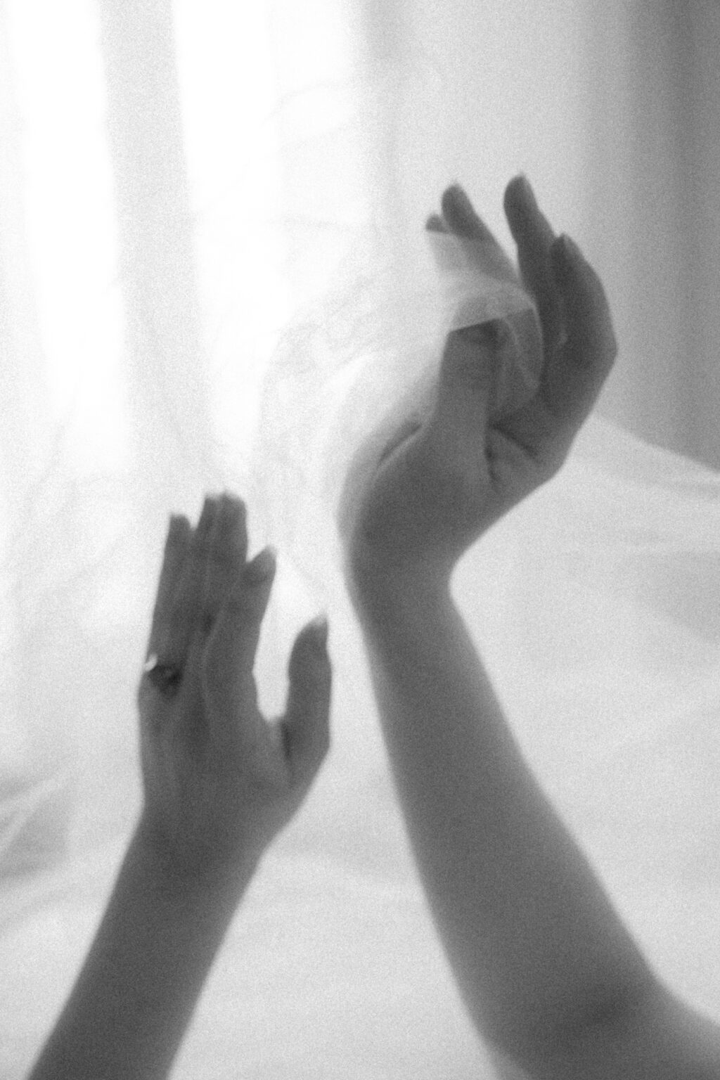 Séance boudoir de la mariée avec mains levées sous un voile blanc, dans une lumière douce et minimaliste.