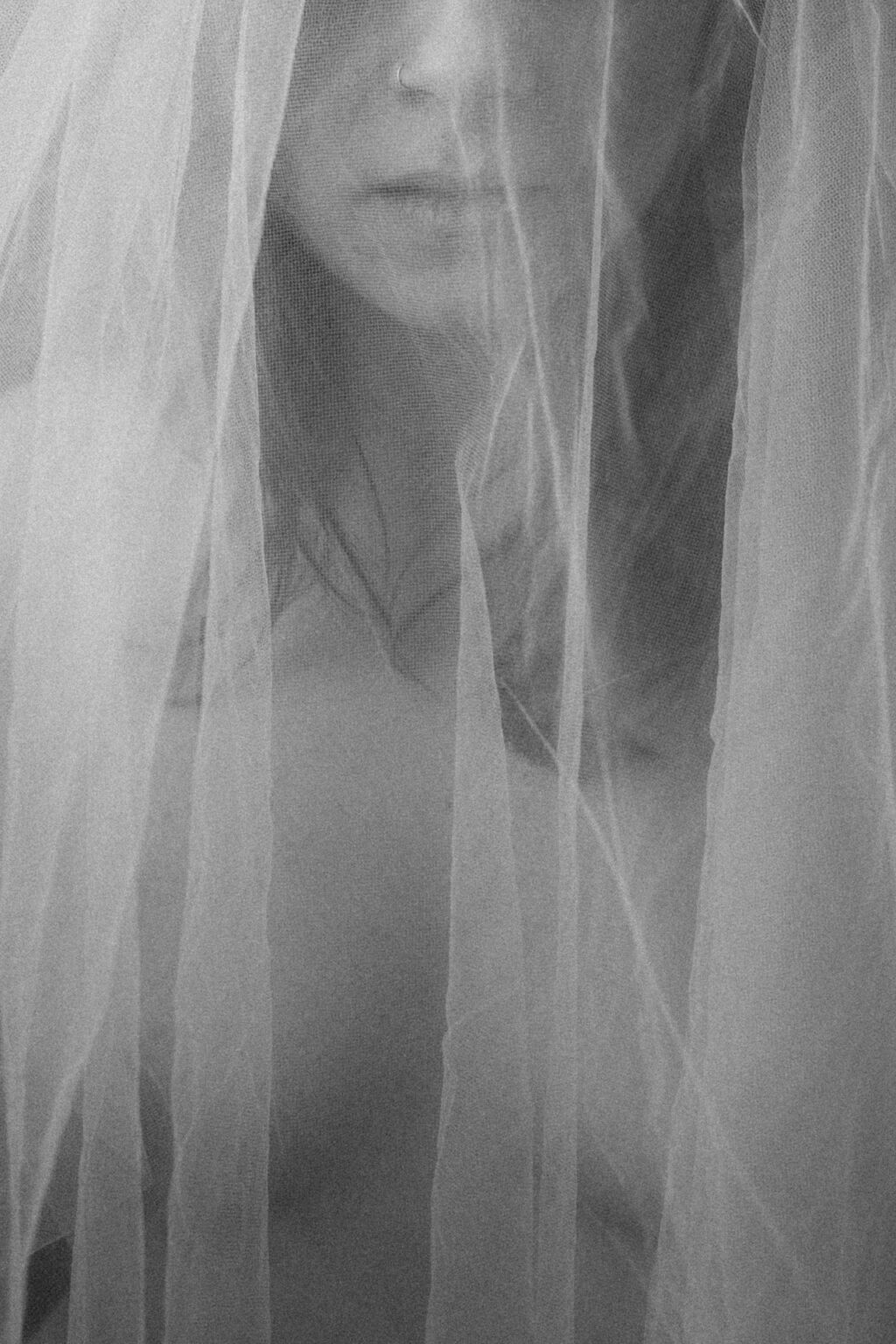 Séance boudoir de la mariée en voile blanc, portrait doux et vaporeux sous un tulle délicat.