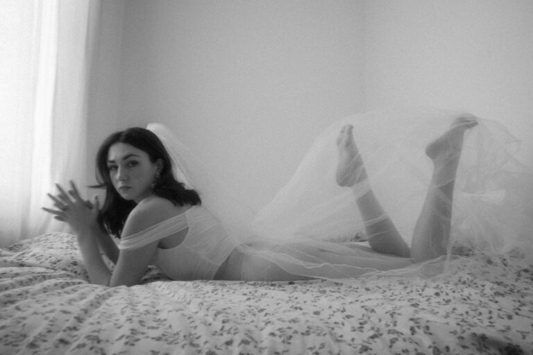 Séance boudoir de la mariée. La mariée est allongée sur un lit avec son voile dans une composition noir et blanc élégante.