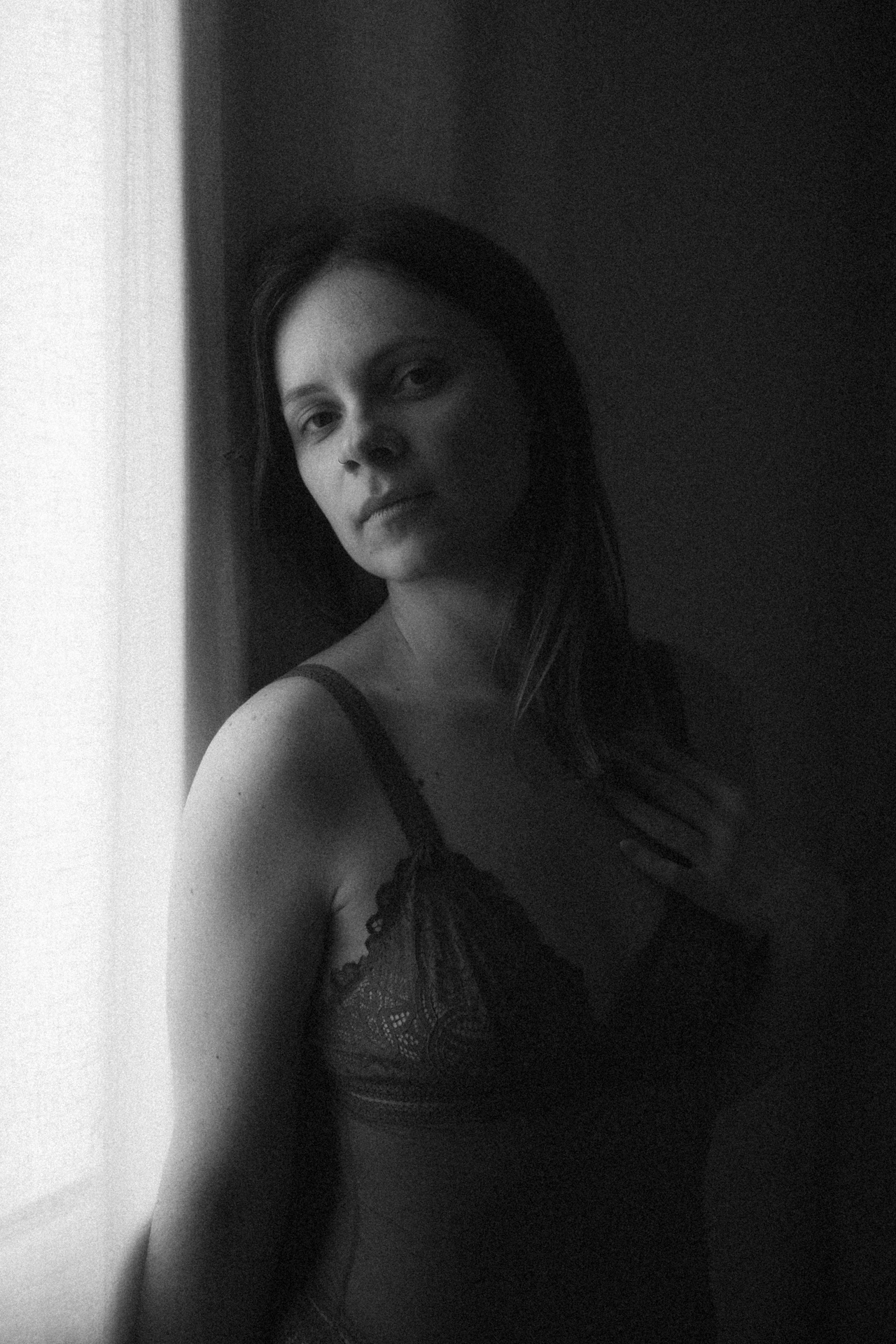 Séance boudoir en Lorraine en noir et blanc, portrait intime près d’une fenêtre avec jeux d’ombre et de lumière.