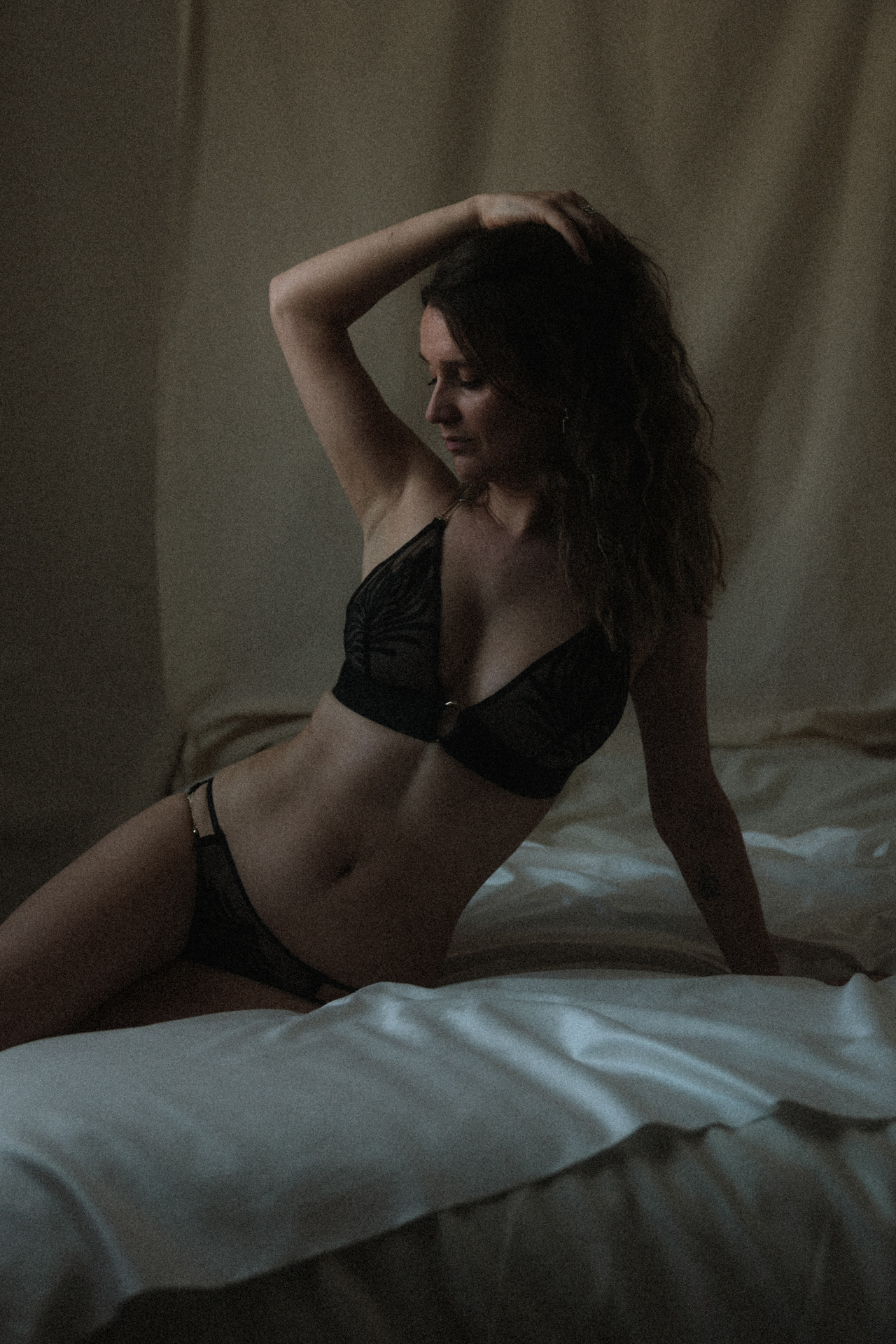 Séance boudoir à Metz en lingerie noire, portrait intime sur un lit dans une atmosphère feutrée.