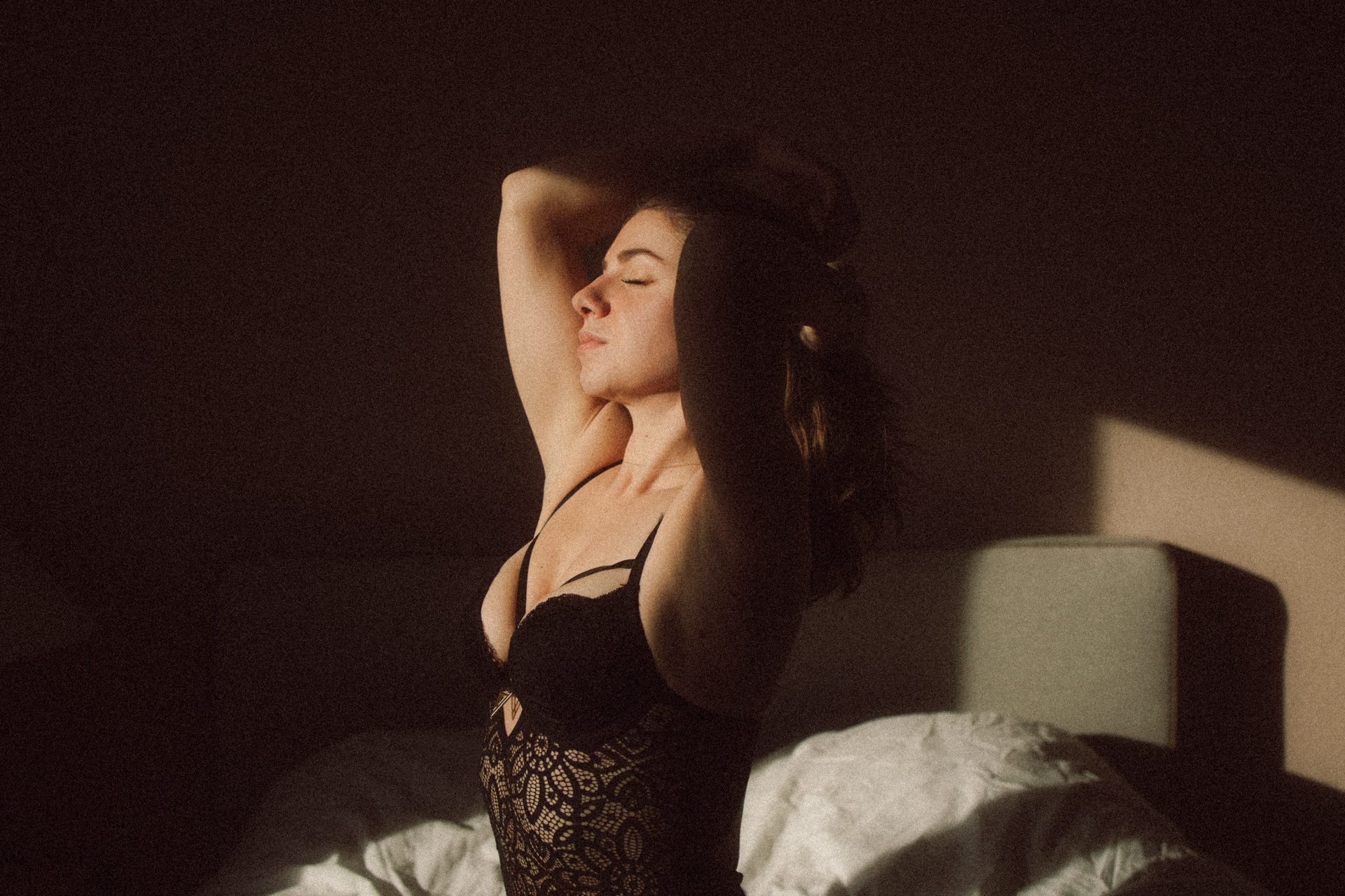 Séance boudoir à Metz, femme portant un body assise sur un lit dans une ambiance cinématographique.