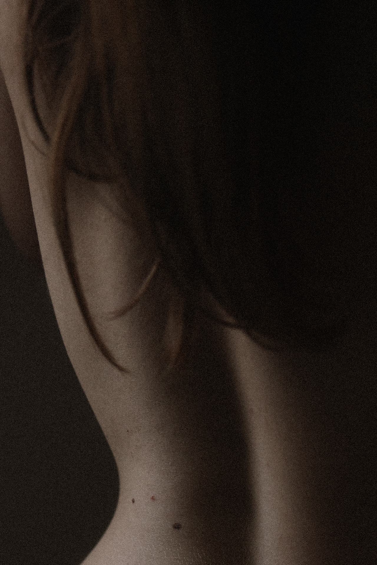 Séance boudoir en Moselle avec détail du dos nu dans une lumière sombre et intime.