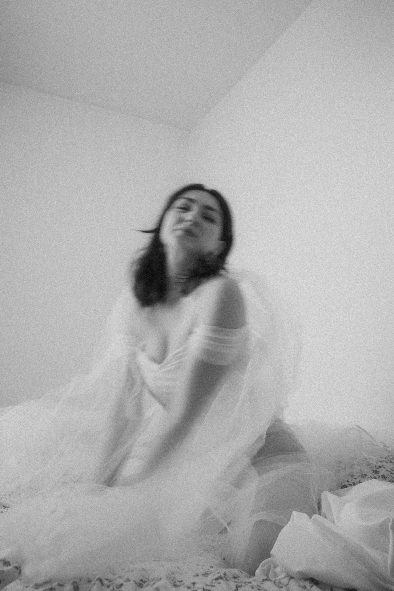 Séance boudoir de la mariée artistique. La mariée est assise sur le lit et joue avec son voile dans une ambiance douce
