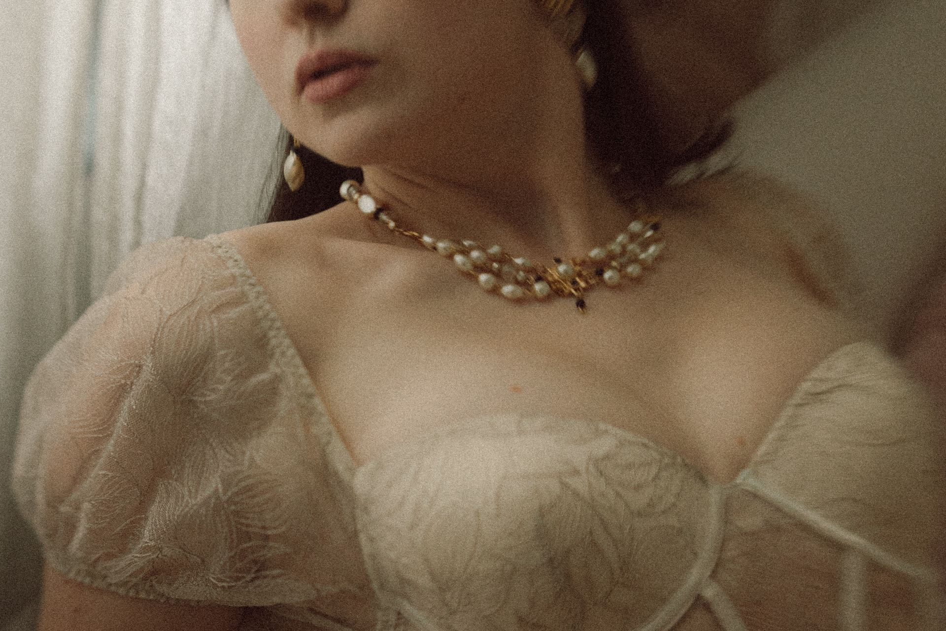 Détail d’une robe de mariée brodée et d’un collier de perles, dans une lumière douce et raffinée lors d'une séance boudoir de la mariée.
